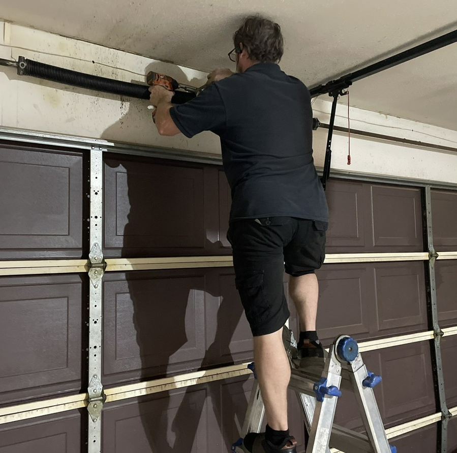 Local garage door repair technicians from Johnstown, Ohio servicing a residential garage door with specialized tools, showcasing professional and branded service.